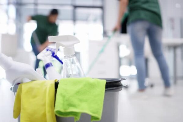4k video footage detergents in a bucket on the floor of an office with two women cleaning in the background